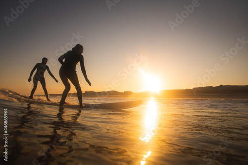 2 female surfers catch a wave at sunrise