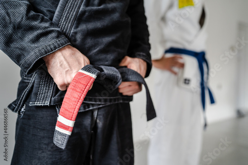 Side view of hand of unknown caucasian man in kimono gi standing while holding black bjj belt brazilian jiu jitsu concept copy space photo