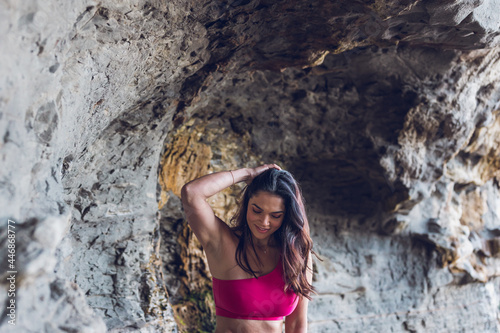 Woman wearing hot pink gym clothes standing by the beach cliffs.