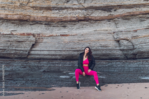 Woman wearing hot pink gym clothes sitting on the rocks at the beach.
