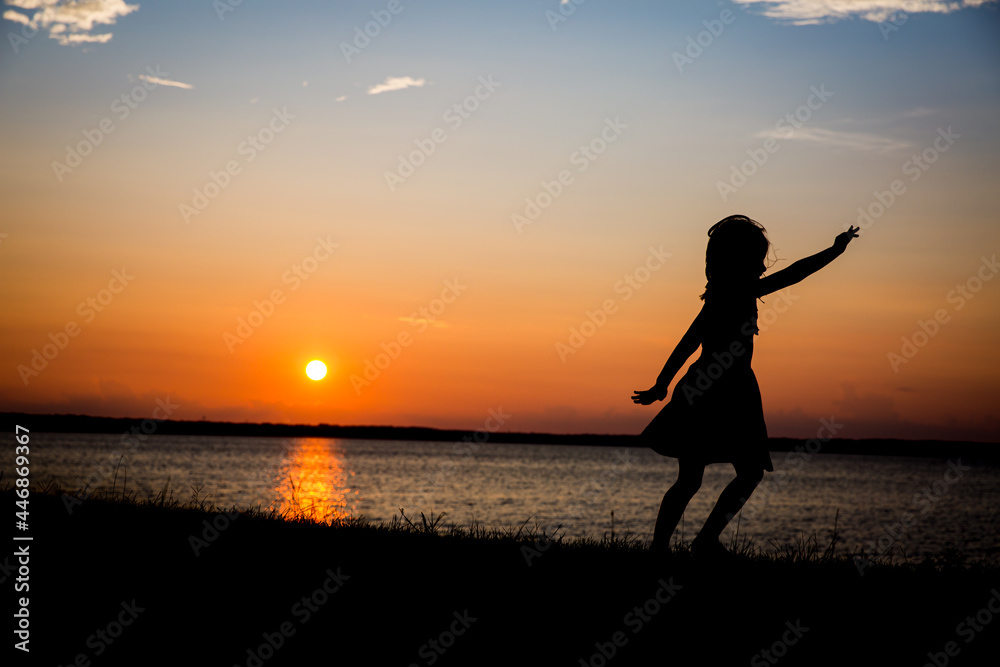 Silhouette of young girl dancing and twirling in the sunset