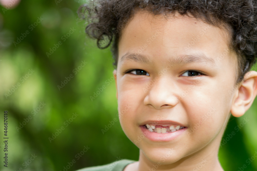Outdoor portrait of a cute smiling boy with curly hair, he is changing his teeth
