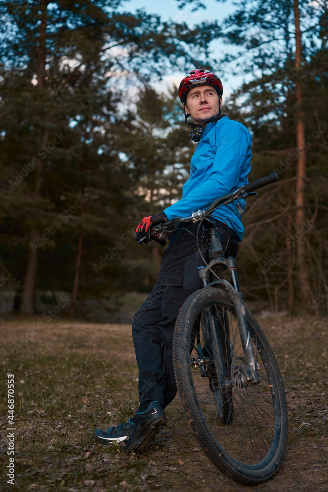 Obraz premium Man wearing bicycle helmet standing in forest, spending free vacation time on a bicycle trip in a forest.