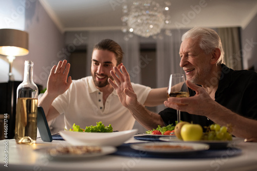 Grandfather and grandson greeting online relative during dinner photo