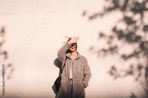 Young woman shielding eyes standing against wall in city