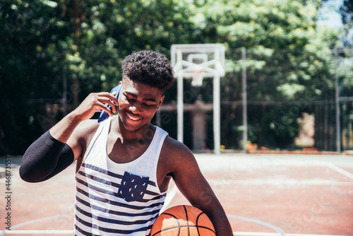 Portrait of a black African-American boy speaking with his mobile phone on an urban basketball court. photo