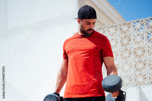 Muscular young man lifting weights outside