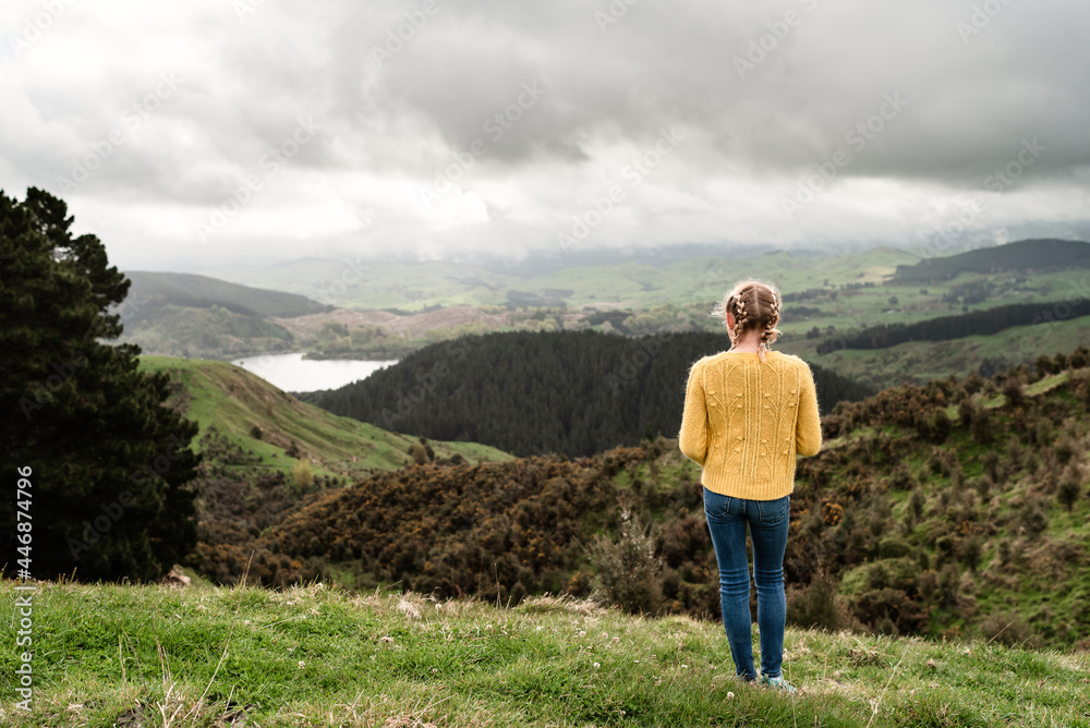 Tween girl in yellow sweater looking at lake from hillside in New Zealand Tween girl in yellow sweater looking at lake from hillside in New Zealand