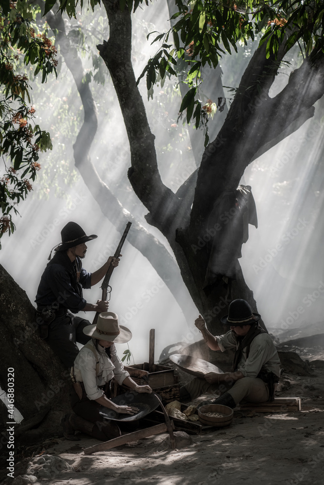 One cowboy with cowgirl are processing to find golds after panning for golds. And another cowboy stand with gun as safety guard. Cowboy concept. One cowboy with cowgirl are processing to find golds after panning for golds. And another cowboy stand with gun as safety guard. Cowboy concept.