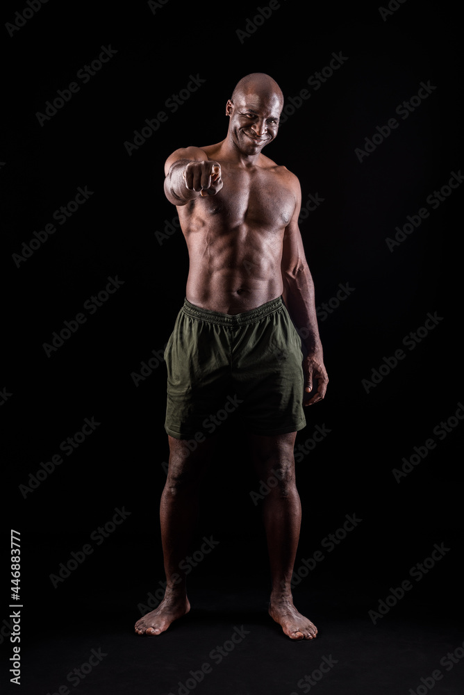 Black muscular man smiling standing and pointing at camera on a black background