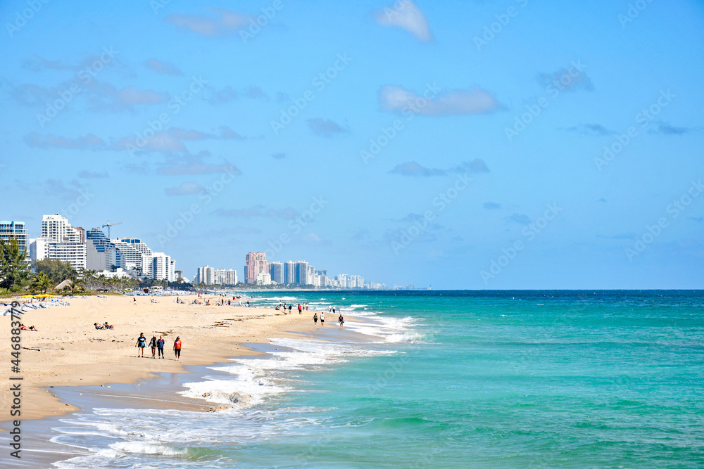 Tourists enjoying a walk along the shoreline with condos in the background in Ft Lauderdale beach Florida	