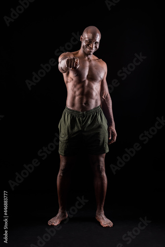 Black muscular man smiling standing and pointing at camera on a black background