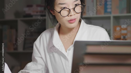 Asian woman wearing glasses working at night, finding documents and looking at laptop, rechecking information. Working hard at home, working from home concept photo