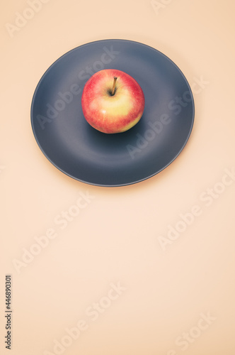 Vertical shot of fresh apple on a black round plate isolated on a pink background photo