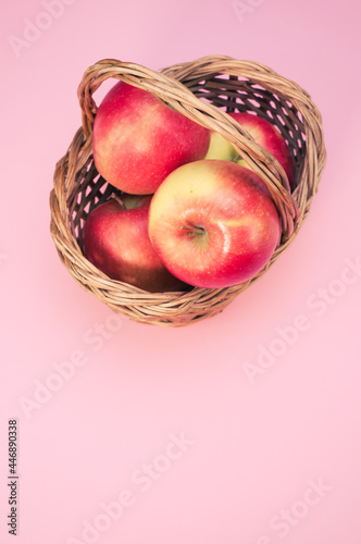 Vertical shot of fresh apples on a woven basket isolated on a pink background with copyspace photo