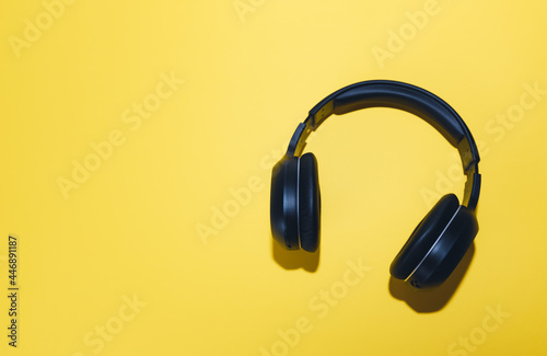 Black wireless headphones isolated on a yellow background. 