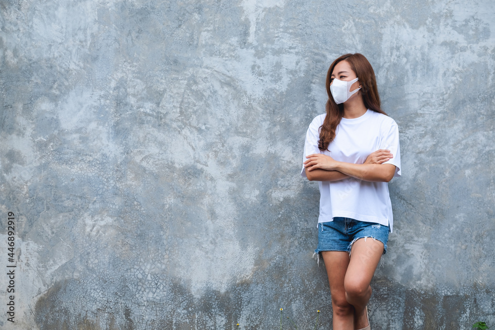 Portrait image of a woman wearing protective face mask standing in front of concrete wall background for Health care and Covid-19 concept