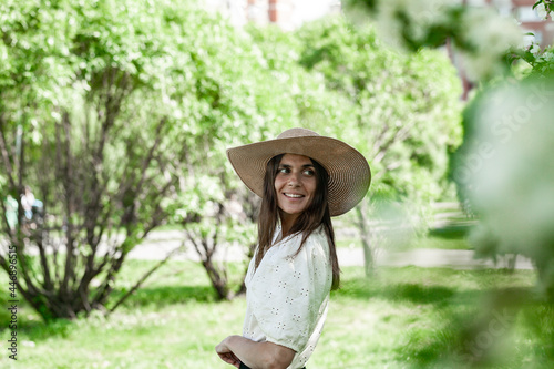 Portrait pretty and attractive female in a straw hat. Young lady in on a spring park background. Cute smiling and happy young woman. Beautiful model on the white blouse. Life style