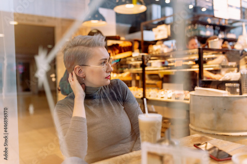 young caucasian blond woman recording audio message with smartphone sitting in cafe