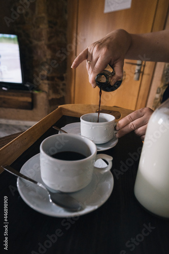 overhead shot of hands pouring coffee with milk in glass bottles over a cup on a wooden tray