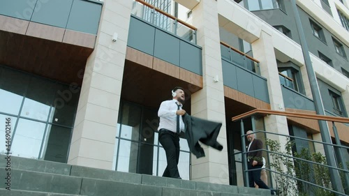 Crazy businessman is dancing outdoors near office building listening to music through headphones relaxing celebrating career success on sumemr day photo