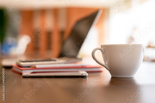 Blurred of cup of hot coffee on wooden table with computer