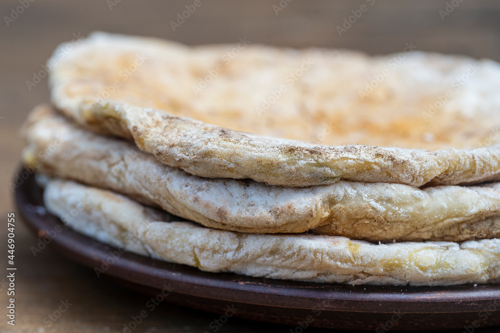 Baked dough tortilla with cottage cheese and herbs in a ceramic plate on a wooden table, close up