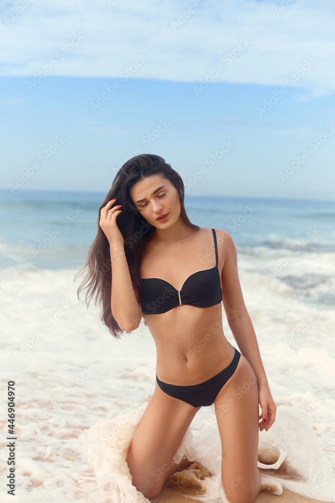 Beautiful luxury slim girl in a black bikini on the beach the ocean. Beauty woman with sexy tanned body, flat stomach, perfect figure. Rest on a tropical island.