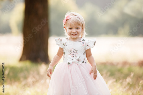 Portrait of a little beautiful girl on nature on summer day vacation. child in dress is playing in the green park at the sunset time. The concept of family holiday and time together