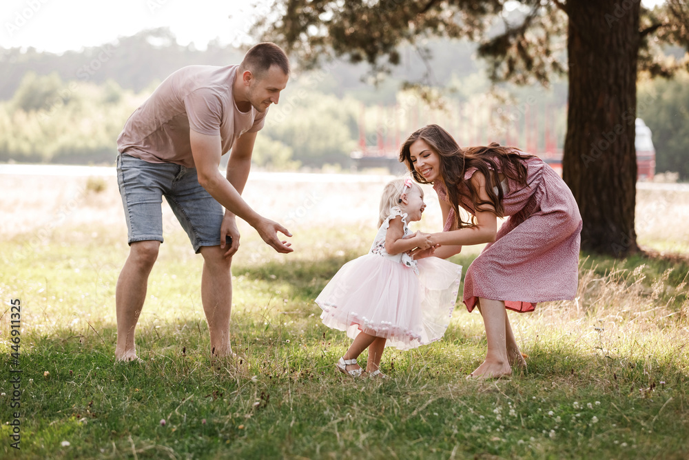 Selective focus. Happy family in the park on summer sunny day. Parents is playing with child. Mom, dad, and daughter walk in the field. The concept of a family holiday.