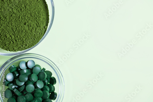 Chlorella powder and spirulina tablets on a green background. Organic food supplement. Copy space, top view, flat lay.