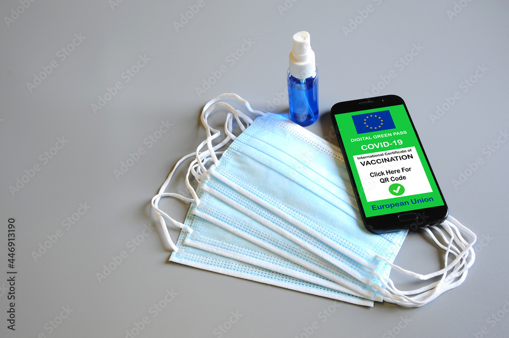 The digital green pass of the European Union on the screen of a smartphone. Covid or Coronavirus vaccine certificate, with protective masks and disinfectant spray