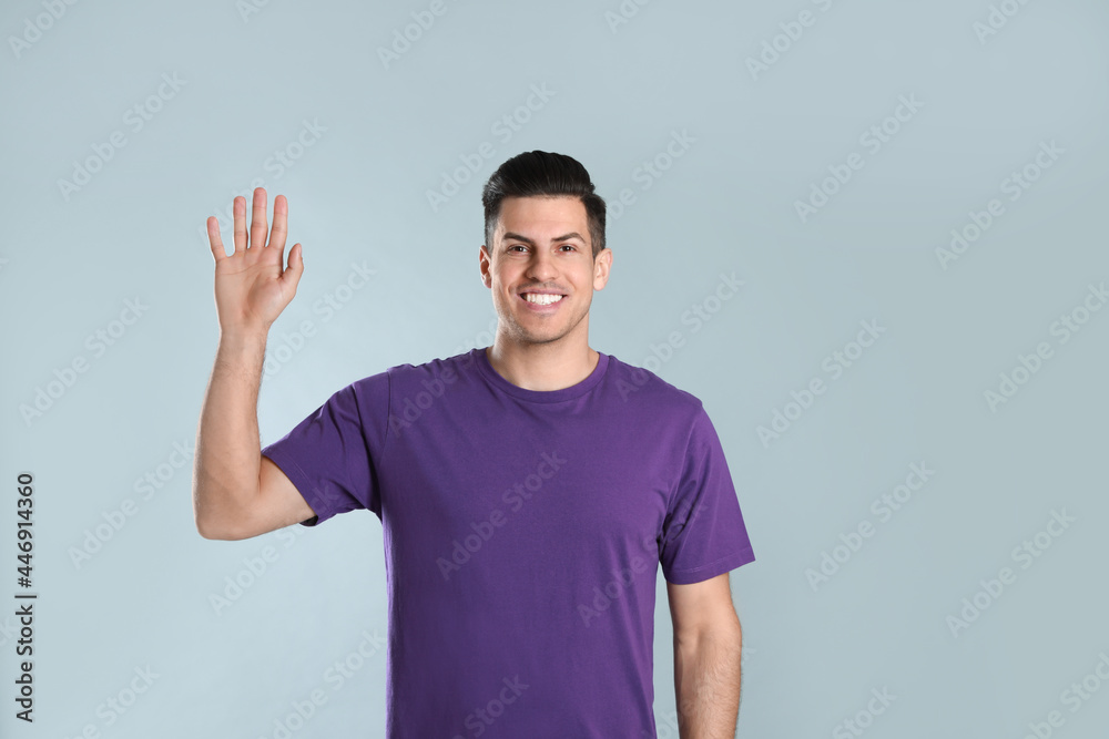 Cheerful man waving to say hello on grey background Cheerful man waving to say hello on grey background