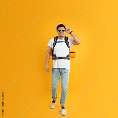 Male tourist with travel backpack on yellow background