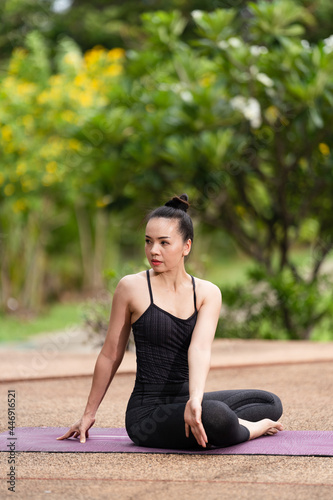 A confident middle-aged Asian woman in sports outfit doing yoga exercise on the yoga mat outdoor in the backyard in the morning. Young woman doing yoga exercise outdoor in nature public park