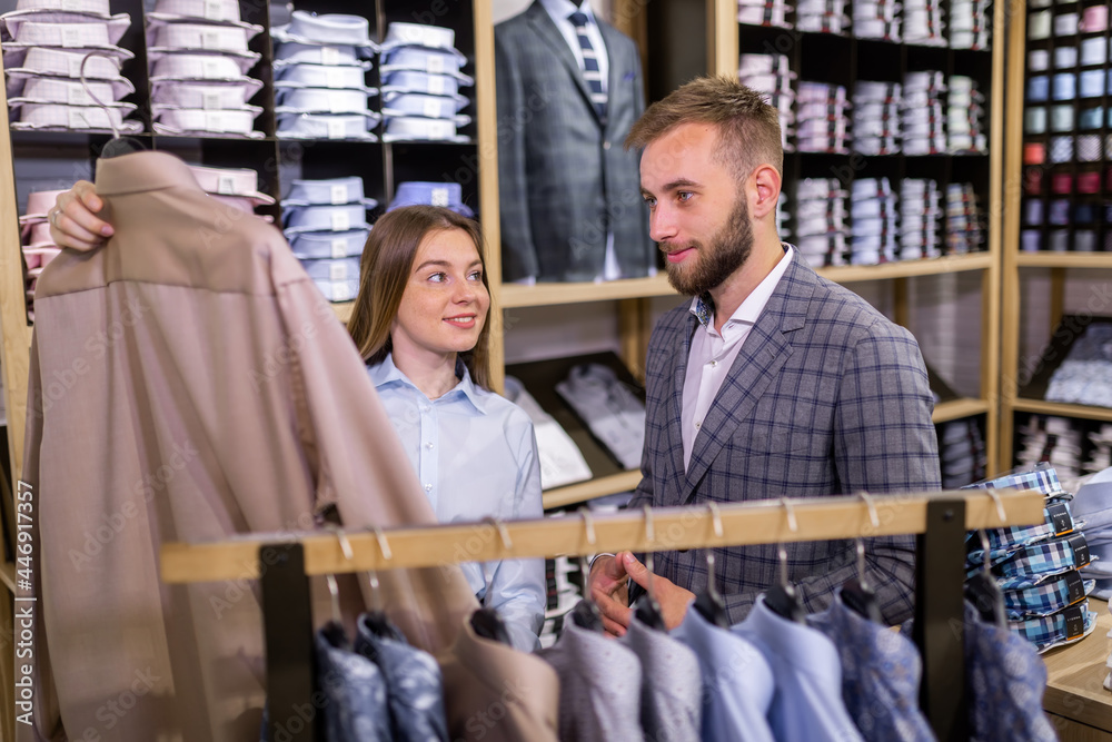 Beautiful elegant girl presents a business style shirt to a confident man in a men's clothing store.