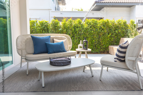 outdoor furniture rattan chairs, table and blue pillow by the home patio. Beautiful and cozy home outdoor space.