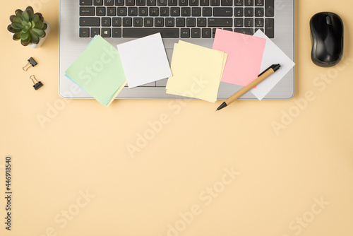 Overhead photo of grey laptop colorful stickers paperclips pen computer mouse and plant isolated on the beige backdrop with copyspace