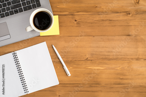 Top view photo of cup of drink yellow sticker note paper on laptop pen and open spiral notepad on isolated wooden table background with blank space