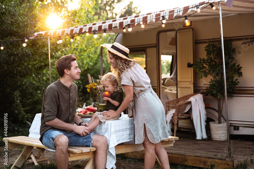 Foto Family vacation in mobile home: young parents travel with small preschool son have picnic on terrace on sunset at rv camper trailer