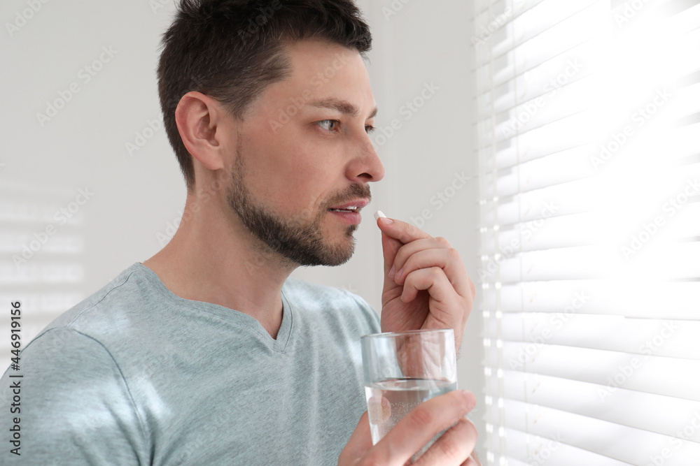Man with glass of water taking pill at home Man with glass of water taking pill at home