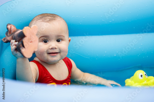 portrait. a small 10-month-old girl in a children's inflatable pool. she smiles and looks at the camera