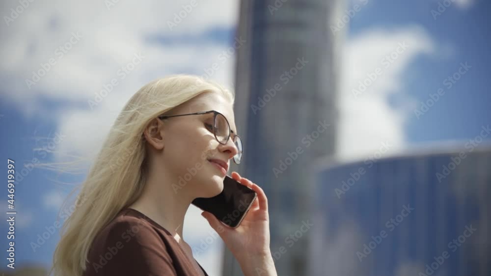 Young blonde woman in glasses talking on the phone against the backdrop of a glazed building. Business and regular work. Big city life. Close-up, slow motion, HD. Young blonde woman in glasses talking on the phone against the backdrop of a glazed building. Business and regular work. Big city life. Close-up, slow motion, HD.