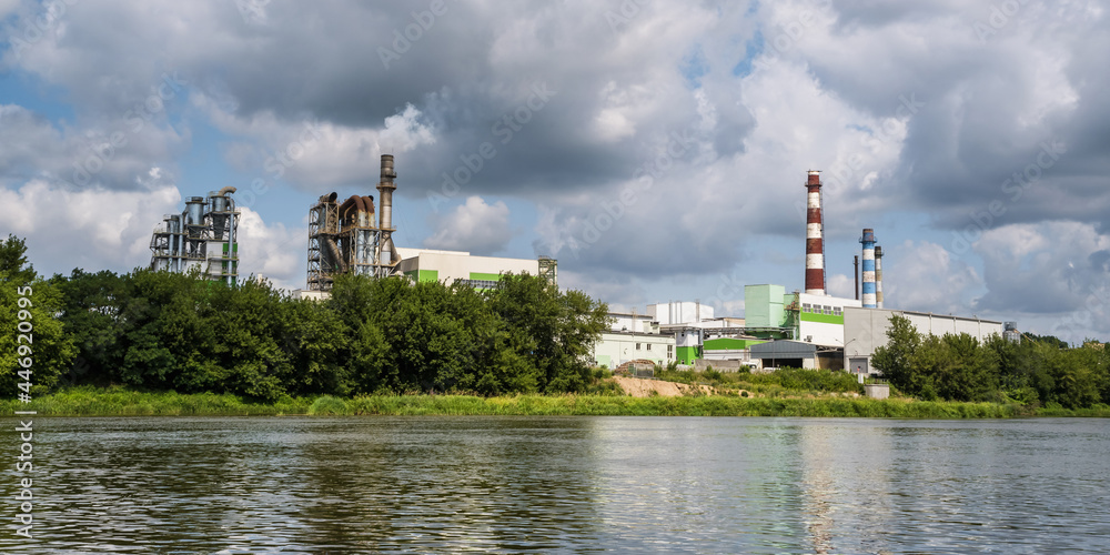 pipes of woodworking enterprise plant sawmill near river. Air pollution concept. Industrial landscape environmental pollution waste of thermal power plant
