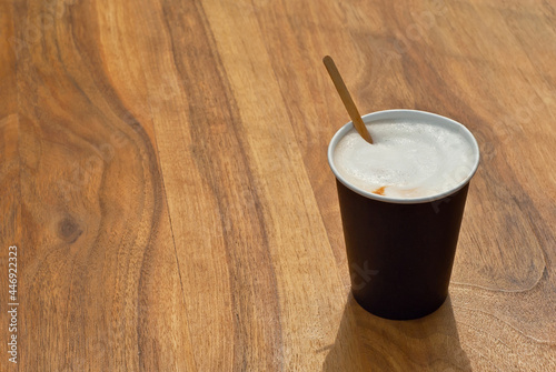 Black paper cup with coffee. Coffee on a wooden table close up.