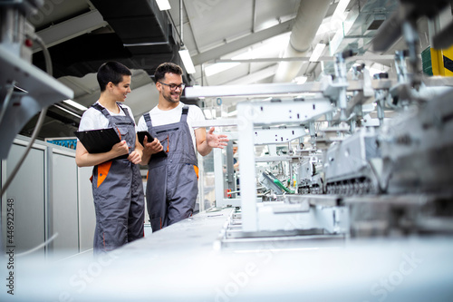 Production line workers controlling manufacturing process of modern packaging industrial machine in factory.