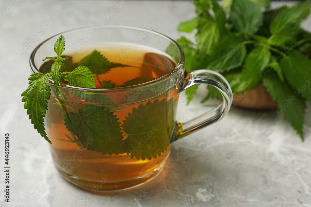 Glass cup of aromatic nettle tea and green leaves on light grey table, closeup Glass cup of aromatic nettle tea and green leaves on light grey table, closeup