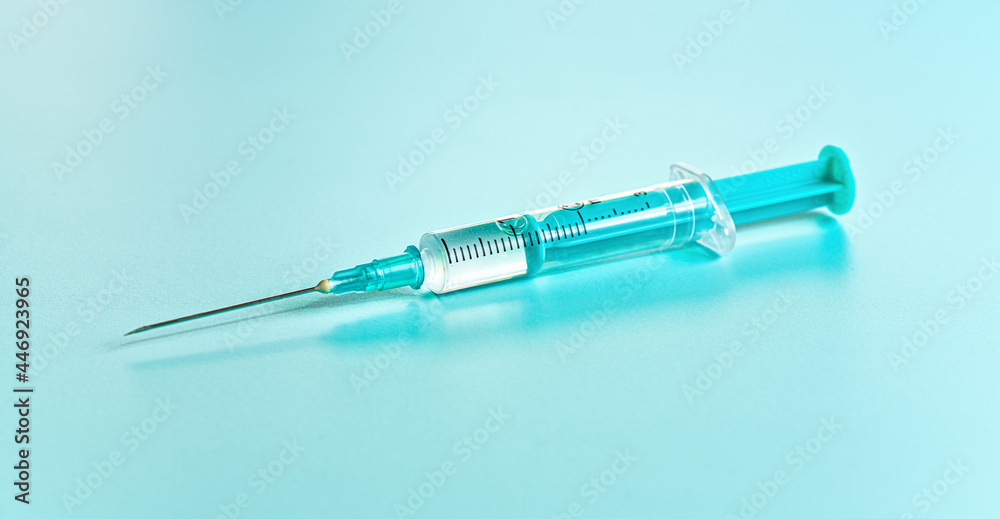 Cyan coloured injection syringe and needle with clear liquid on a board, close-up detail Cyan coloured injection syringe and needle with clear liquid on a board, close-up detail