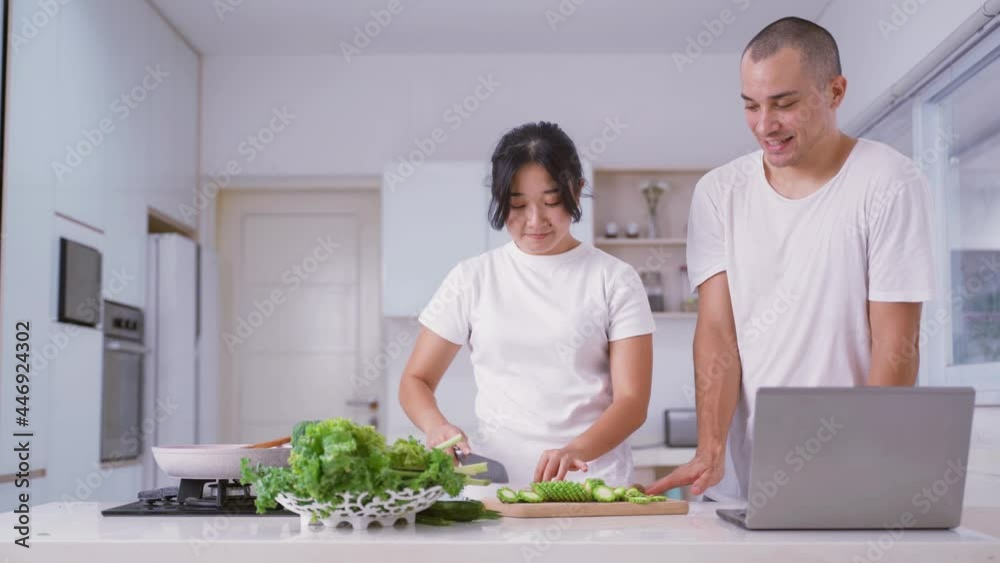 Happy couple cooking vegetable while using laptop Happy couple cooking vegetable while using laptop
