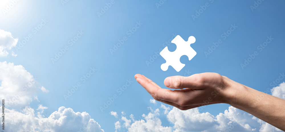 Male hand holding puzzle icon on blue background. pieces representing the merging of two companies or joint venture, partnership, Mergers and acquisition concept.